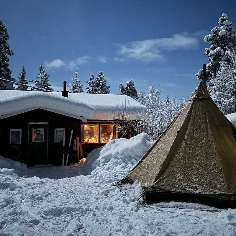 Snow-covered cabin and lavvu tent at Kvikkjokk basecamp on a clear winter night
